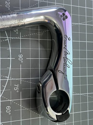 Close-up of a metallic bicycle component with a curved shape and engraved text.